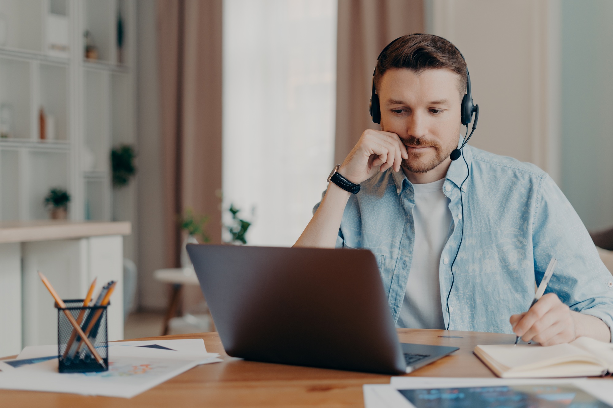 man freelancer listens important info online makes necessary notes in diary works on laptop
